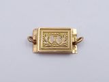 a close up of a gold plated pendant on a white surface