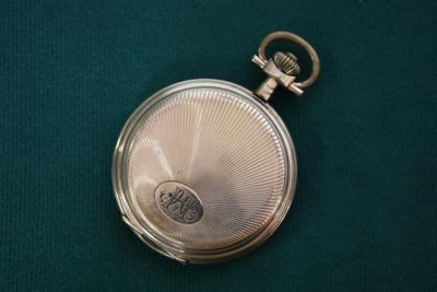 une petite montre de poche en argent posée sur une surface verte