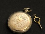 an antique silver pocket watch with a key on a black background