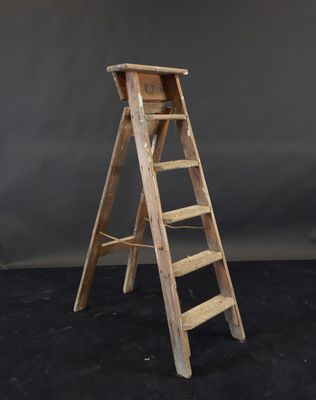 une vieille échelle en bois avec un siège en bois posé sur une surface noire