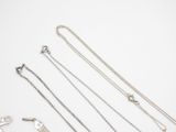 several silver necklaces and a key on a white surface
