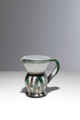 une cruche verte et blanche posée sur une table blanche, sur fond gris