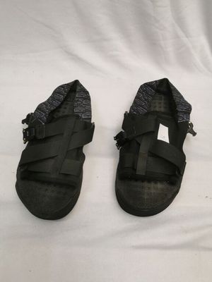 une paire de sandales noires posée sur un lit recouvert d'un drap blanc