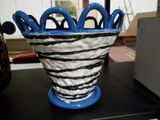 un vase noir et blanc avec des anses bleues posé sur une table noire