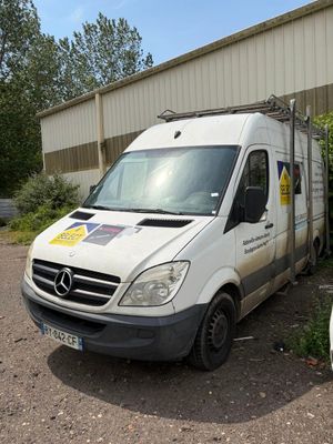 une camionnette blanche garée à côté d'un immeuble, avec une planche de surf sur le toit