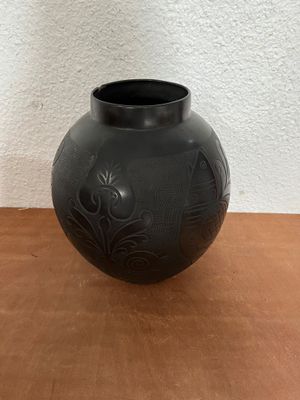 a black vase sitting on a table with a white wall in the background