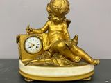 une statue en or représentant un enfant, avec une horloge posée sur une table