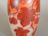 an orange vase with leaves on it sitting on a table