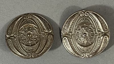 two silver buttons with designs on them sitting on a table