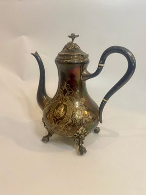 an antique silver tea pot with a blue handle sitting on a white surface