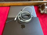 un ordinateur portable MacBook Pro d'Apple avec son chargeur et son câble, posé sur une surface rouge