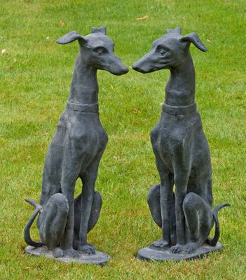 deux statues de lévriers assis l'un sur l'autre dans l'herbe
