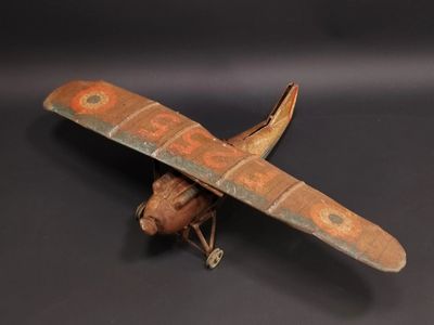 une vieille maquette en bois représentant un petit avion, posée sur une surface noire