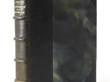 an old book with a black cover sitting on top of a white table