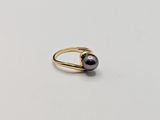 a black pearl and gold ring on a white surface