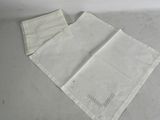 two white linen napkins with embroidered designs on them sitting on a table