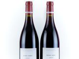 two bottles of red wine sitting next to each other on a white surface