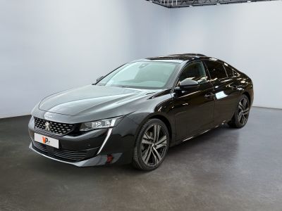 La voiture noire est garée dans une grande pièce aux murs blancs.