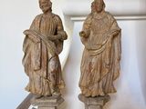 pair of carved statues of two men on pedestals in front of a wall