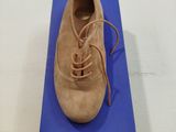 chaussures beiges en daim à lacets, posées sur une boîte bleue, sur une surface blanche