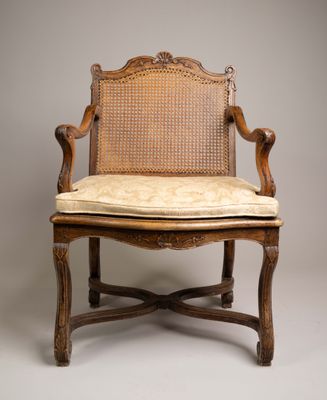 une vieille chaise avec un dossier en rotin et un coussin posé dessus