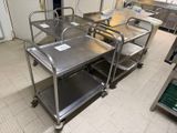 many stainless steel tables in a kitchen with a refrigerator in the background