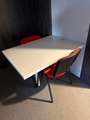 une table blanche avec deux chaises rouges dans un coin de la pièce