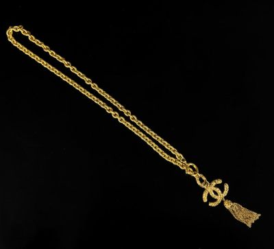 a gold necklace with a tassel on a black background