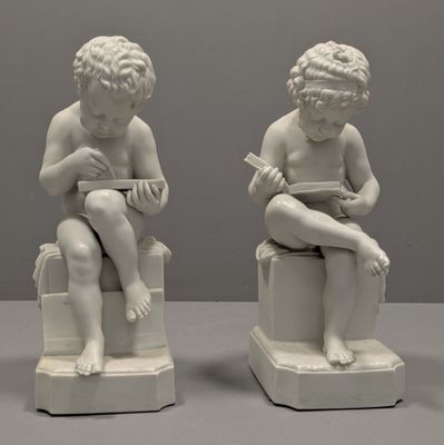 une paire de statues blanches représentant des enfants assis sur des tabourets en train de lire un livre