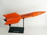 une maquette orange d'un avion de chasse posée sur un socle noir
