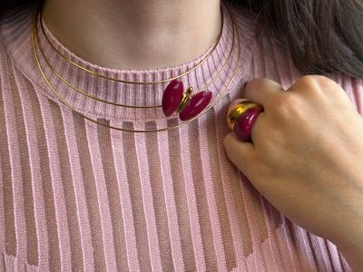 une femme portant un pull rose et un collier en or orné d'une fleur rouge