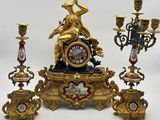 une horloge en or posée sur une table, à côté de trois chandeliers
