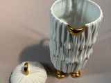 a white cup with a gold handle next to a white cup