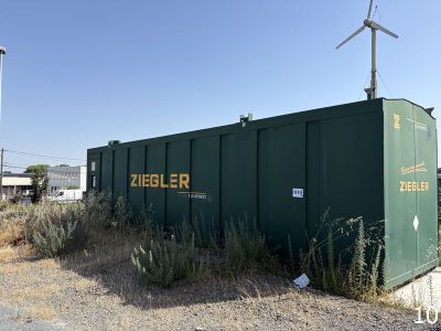un conteneur vert posé au milieu d'un champ de terre battue
