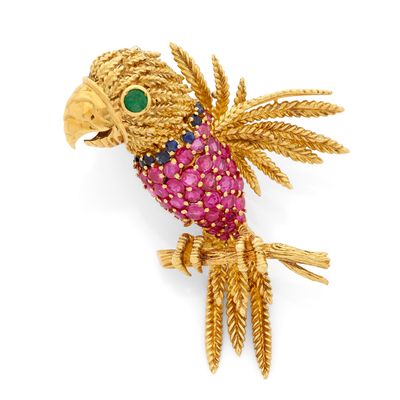 un gros plan sur une broche en forme d'oiseau en or, ornée de pierres roses et vertes