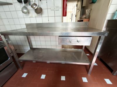 une table en acier inoxydable dans une cuisine, avec une cuisinière en arrière-plan