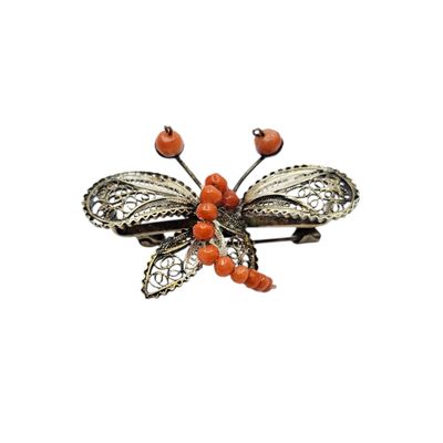 a close up of a butterfly brooch with red berries on it