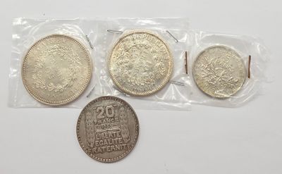 trois pièces d'argent dans des sachets en plastique, posées sur une surface blanche