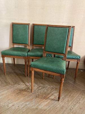 quatre fauteuils en cuir vert posés sur un parquet, près d'un mur