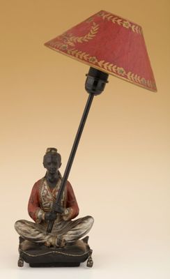 une statue représentant un homme assis sur un tabouret sur lequel est posée une lampe