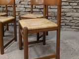 two wooden chairs sitting next to each other in front of a stone wall