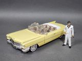 toy man in white suit standing next to a yellow car with a skeleton in the trunk