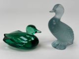 two glass ducks sitting next to each other on a white surface