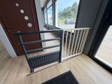 une barrière de sécurité pour bébé placée devant une porte, avec un paillasson noir