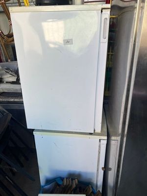 a white refrigerator sitting in a garage next to a trash can