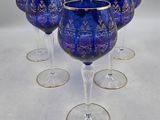 six verres à vin bleus bordés d'or, posés sur un fond blanc