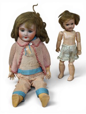 two old dolls sitting next to each other on a white surface