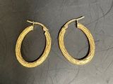 une paire de boucles d'oreilles créoles dorées sur un fond noir