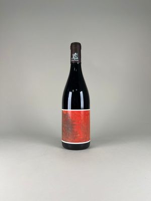 the bottle of red wine is sitting on a white surface