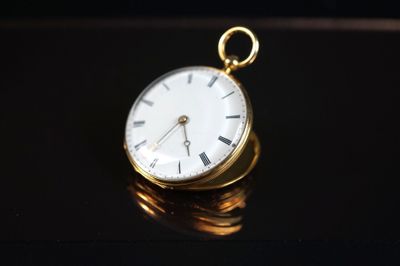 une montre de poche en or posée sur une pile de pièces de monnaie